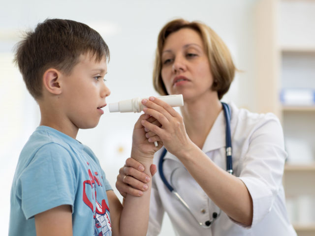 Little boy blowing to peak metr medical device. Doctor examining child's lungs