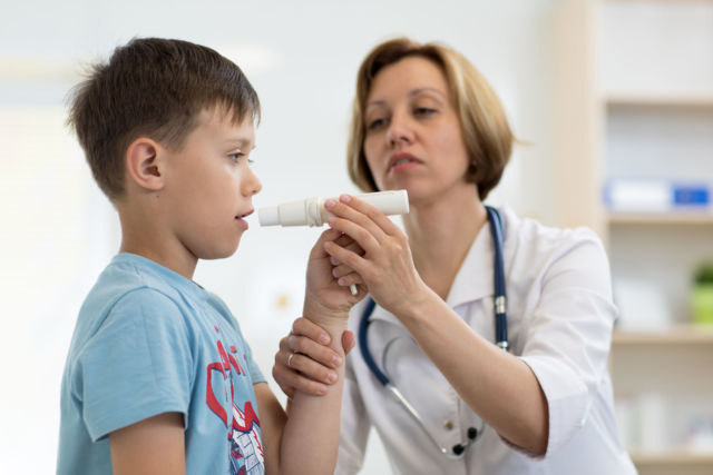 Little boy blowing to peak metr medical device. Doctor examining child's lungs