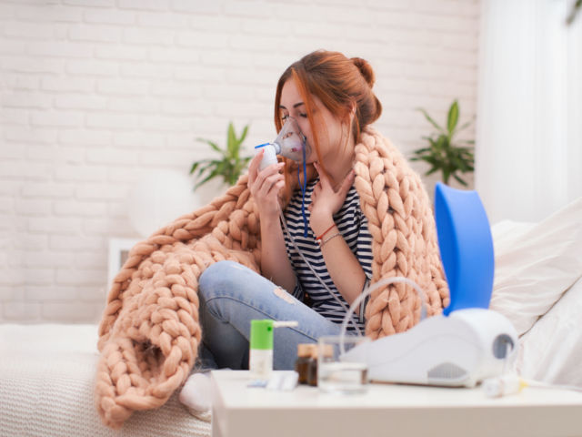 Young woman doing inhalation with a nebulizer at home